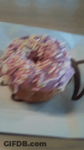A Donut With Pink Frosting And Sprinkles On Top GIF