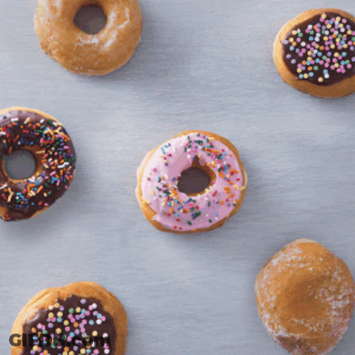 A Donut With Pink Frosting Is Surrounded By Other Donuts GIF
