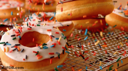 A Donut With White Frosting And Sprinkles Is Sitting On A Wire Rack GIF