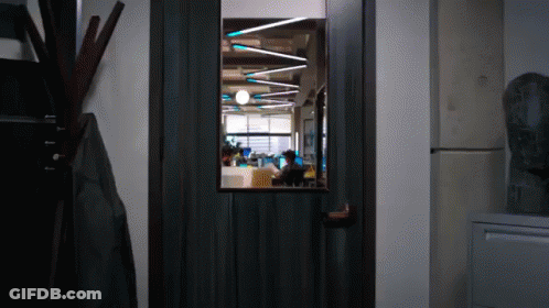 A Door With A View Of A Room With People Working GIF