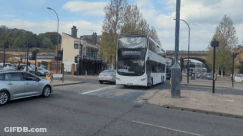A Double Decker Bus Is Driving Down The Road GIF