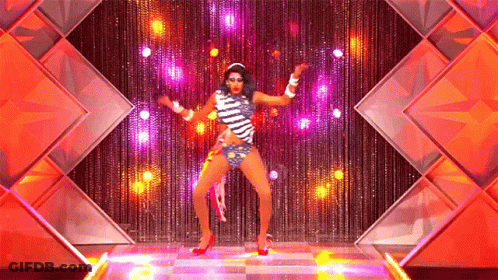A Drag Queen Is Dancing On A Stage In Front Of A Curtain GIF