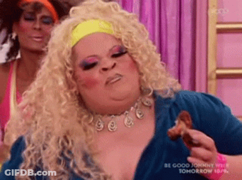 A Drag Queen Is Eating A Piece Of Chicken While A Woman Looks On . GIF