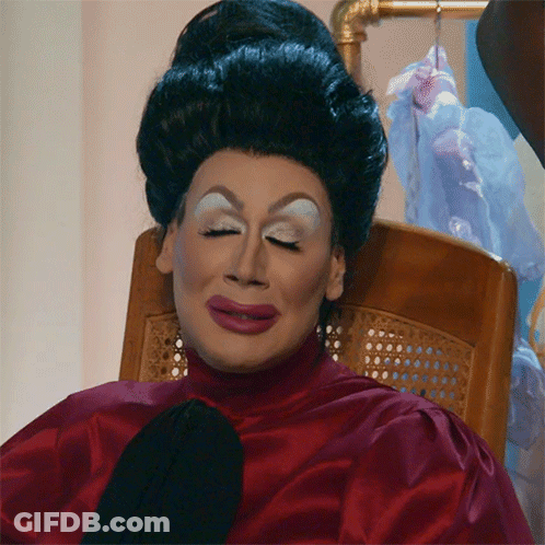 Drag Queen Sitting In Red Top And Black Tie GIF