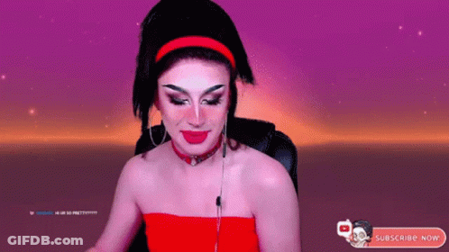 A Drag Queen Is Sitting In Front Of A Purple Background And Holding A Cotton Candy Bar . GIF