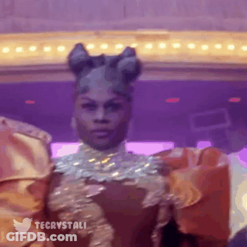 Drag Queen Standing In Front Of Purple Wall And Twitter Logo GIF
