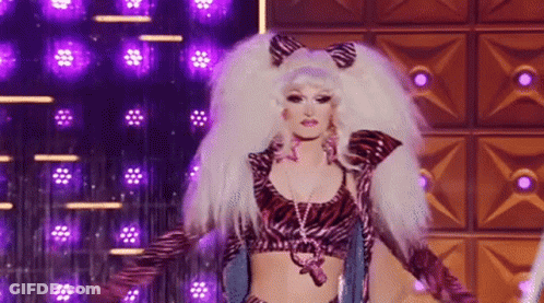 A Drag Queen Is Standing On A Stage Wearing A Zebra Print Top And Gloves . GIF