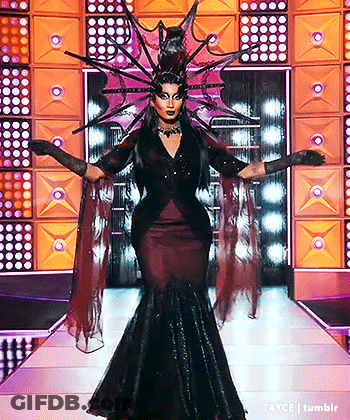 A Drag Queen Is Walking Down A Runway Wearing A Costume That Looks Like A Witch . GIF