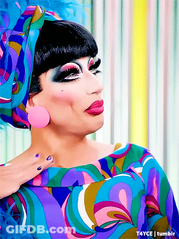 A Drag Queen Is Wearing A Colorful Dress And A Headband GIF