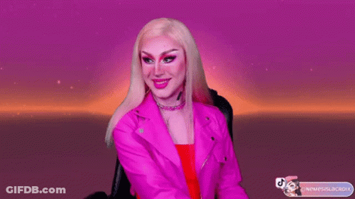 A Drag Queen Is Wearing A Pink Jacket And Earrings GIF