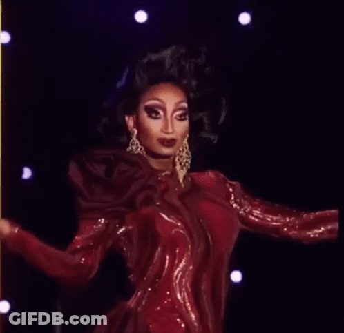 A Drag Queen Is Wearing A Red Dress And Earrings While Standing On A Stage . GIF