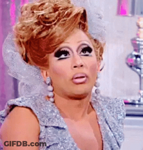 A Drag Queen Is Wearing A Silver Dress And Earrings And Making A Surprised Face . GIF