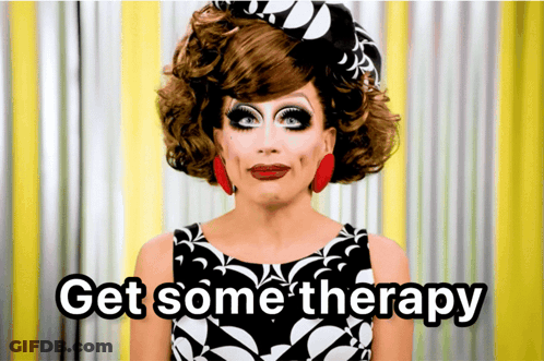 A Drag Queen Says " Get Some Therapy " In Front Of A Yellow Curtain GIF