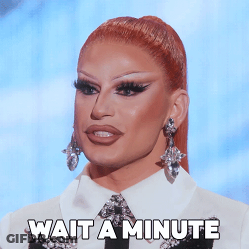A Drag Queen Says Wait A Minute While Wearing Earrings And A White Shirt GIF