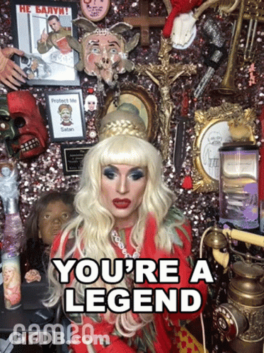 A Drag Queen Says " You 'Re A Legend " In Front Of A Wall Of Memorabilia GIF