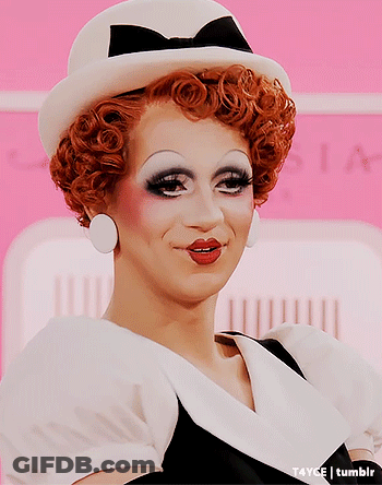 A Drag Queen Wearing A White Hat And Earrings GIF
