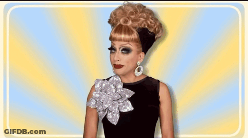 A Drag Queen Wearing A Wig And Earrings Is Smiling GIF