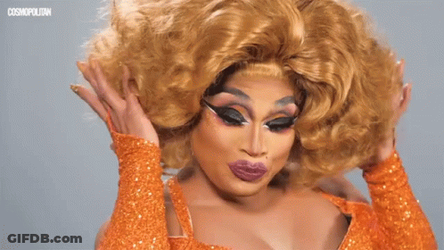 A Drag Queen Wearing An Orange Dress And Gloves GIF