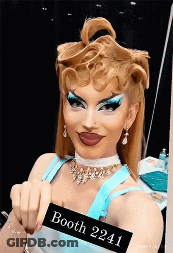 A Drag Queen With A Sign That Says Booth 2241 GIF