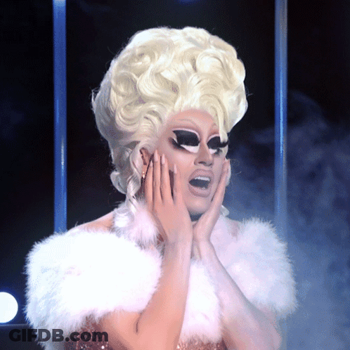 A Drag Queen With Blonde Hair And A White Fur Collar GIF