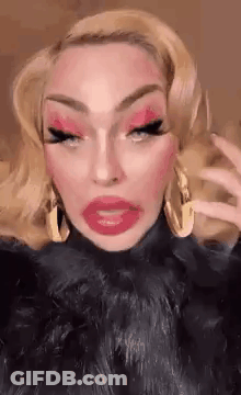 A Drag Queen With Blonde Hair And Red Lips Is Wearing A Black Fur Coat . GIF