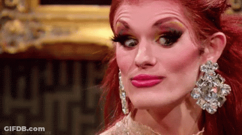A Drag Queen With Red Hair And Earrings Is Making A Face . GIF