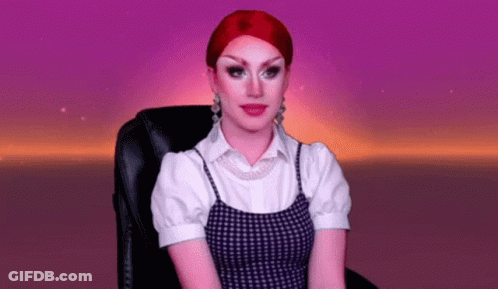 A Drag Queen With Red Hair Is Sitting In A Chair With A Purple Background . GIF