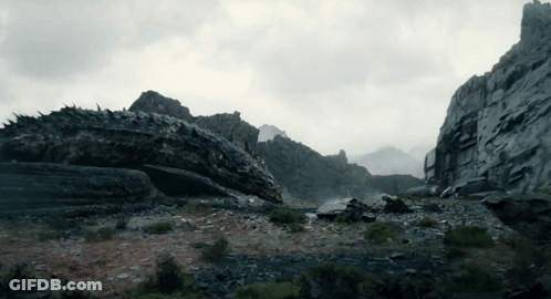 A Dragon Is Laying On The Ground In The Middle Of A Mountain GIF