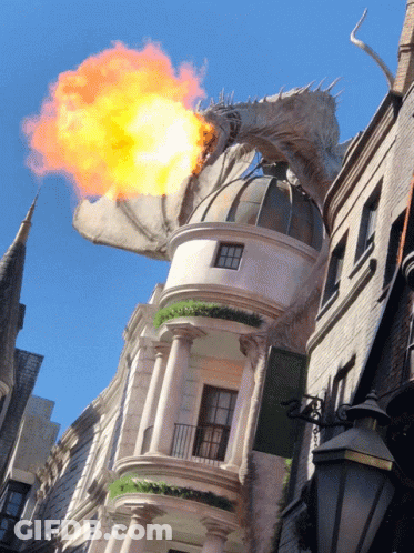 A Dragon With Flames Coming Out Of Its Mouth Is Flying Over A Building GIF