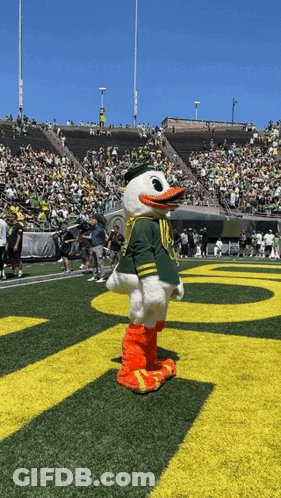 A Duck Mascot Stands On A Field In Front Of A Stadium Full Of People GIF