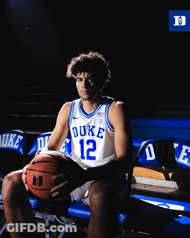 A Duke Basketball Player Sits On A Bench Holding A Ball GIF