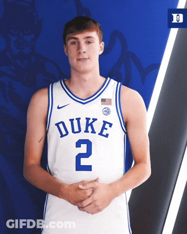 A Duke Basketball Player Stands With His Hands Folded In Front Of A Blue Background GIF