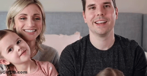 A Family Is Posing For A Picture While Sitting On A Bed And Smiling At The Camera . GIF