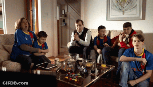 A Family Is Sitting On A Couch Watching A Game And One Of The Boys Is Wearing A Shirt That Says Barcelona GIF