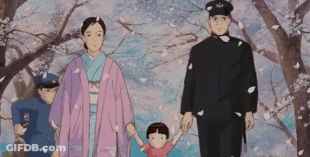 A Family Is Walking Through A Park With Cherry Blossoms Falling From The Trees . GIF