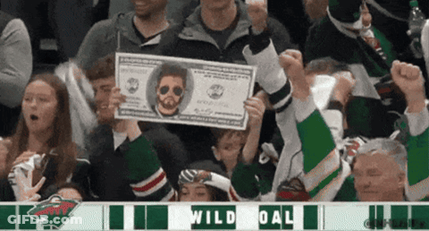 A Fan Holds Up A Dollar Bill With A Picture Of A Man On It In Front Of A Sign That Says Wild Goal GIF