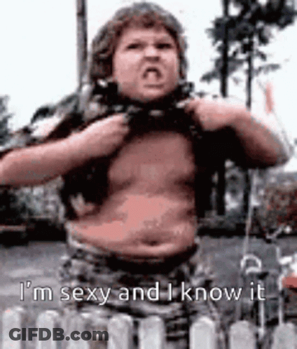 A Fat Boy Is Standing In Front Of A Fence And Taking Off His Shirt While Making A Funny Face . GIF