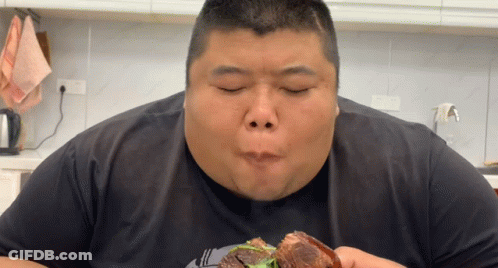 A Fat Man Is Eating A Piece Of Meat In A Kitchen GIF