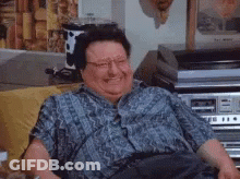 A Fat Man Is Laughing While Sitting On A Couch In A Living Room . GIF