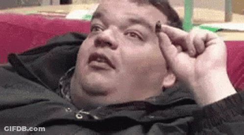 A Fat Man Is Laying On A Couch Holding Something To His Head . GIF