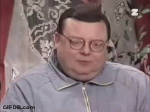 A Fat Man Wearing Glasses And A Blue Jacket Is Sitting In Front Of A Window . GIF