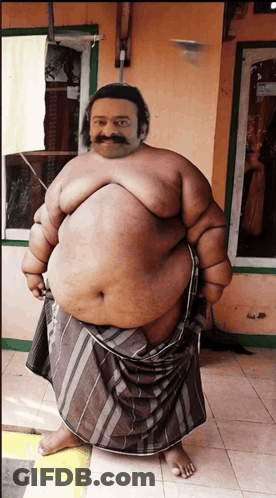 A Fat Man With A Mustache Is Standing In Front Of A Building GIF