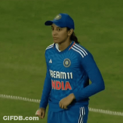 A Female Cricket Player Is Standing On A Field Holding Her Shirt . GIF