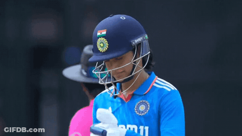 A Female Cricket Player Wearing A Helmet And Gloves Is Looking At Her Phone GIF