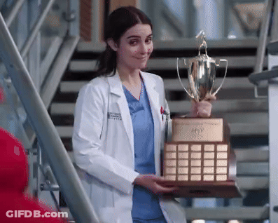 A Female Doctor In A Lab Coat Is Holding A Trophy . GIF