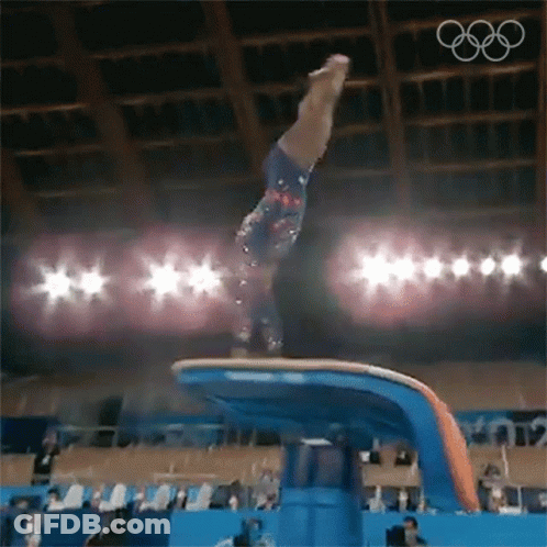 A Female Gymnast Is Doing A Trick On A Balance Beam In Front Of A Crowd . GIF