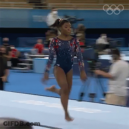 A Female Gymnast Is Doing A Trick On A Mat With The Olympic Rings In The Background . GIF