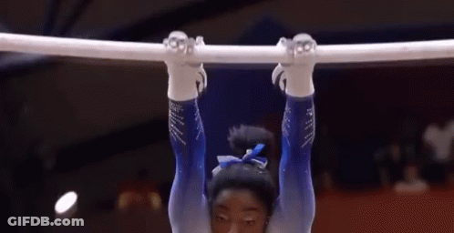 A Female Gymnast Is Hanging Upside Down On A Bar In A Gym . GIF