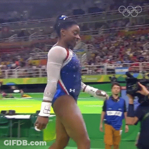 A Female Gymnast Is Walking In Front Of A Crowd While Wearing A Blue And White Leotard . GIF