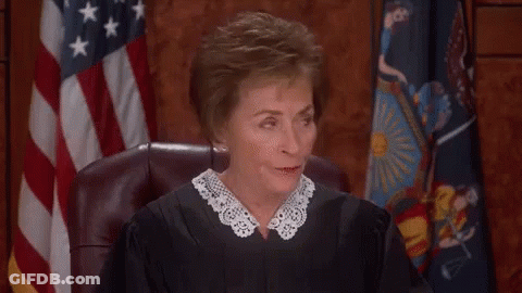 A Female Judge Is Sitting In A Courtroom In Front Of A Flag . GIF